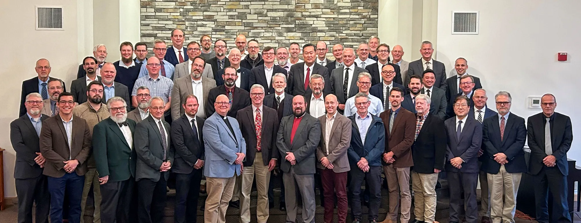 Delegates and observers at the 49th NAPARC annual meeting, gathered in front of a stone wall at Northland Reformed Church in Kansas City, Missouri